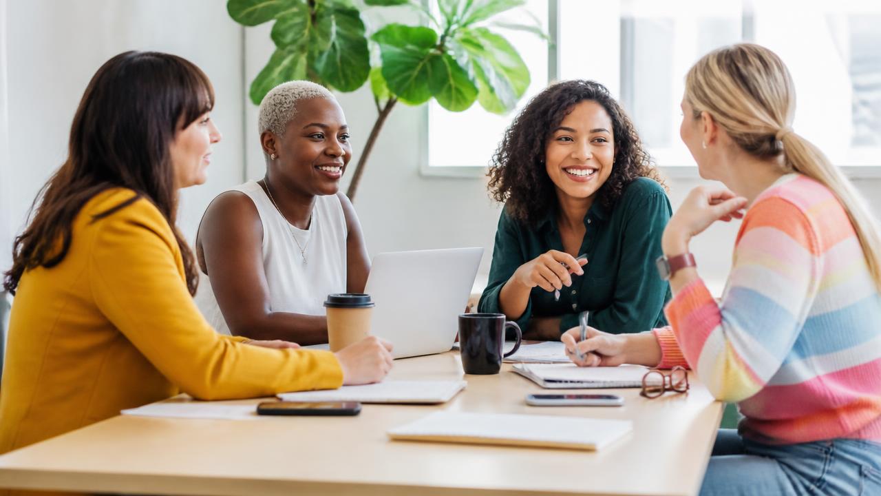 Four women talking together around a table in a bright modern office
